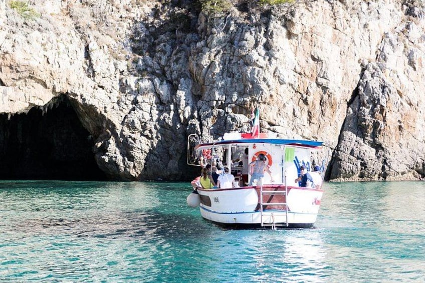 A boat with passengers, a rocky coastline, and a clear blue sea. 4