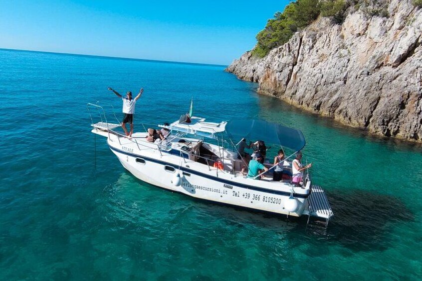 A boat with people on it, surrounded by clear blue water and rocky cliffs. 2