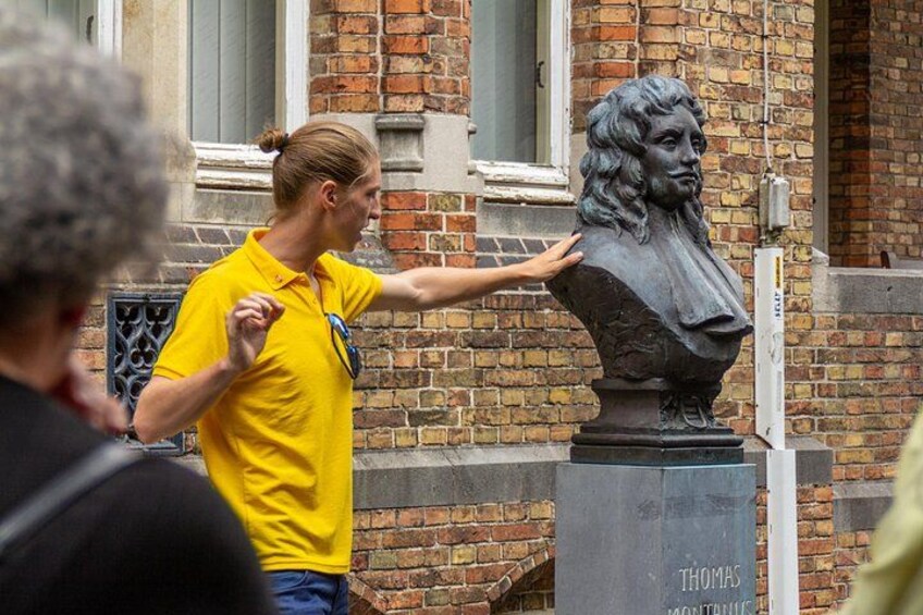 A person in a yellow shirt touching a bust sculpture on a pedestal with the name 'THOMAS' visible. 2