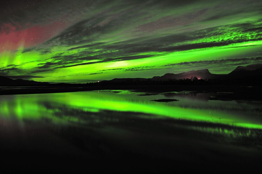 The Northern Lights over a calm lake with mountains in the background. 4
