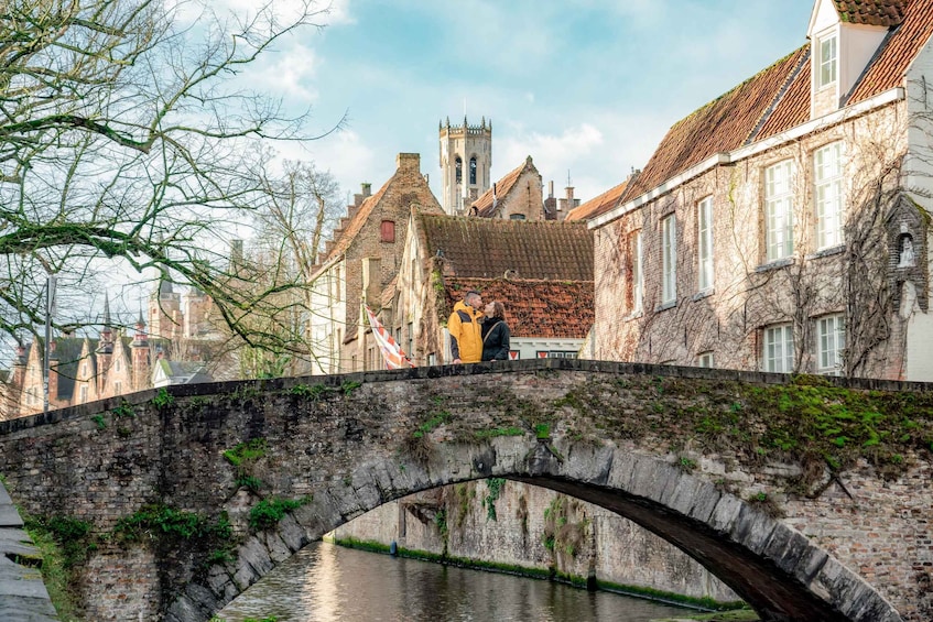 A stone bridge over a canal with buildings and a tower in the background. 4