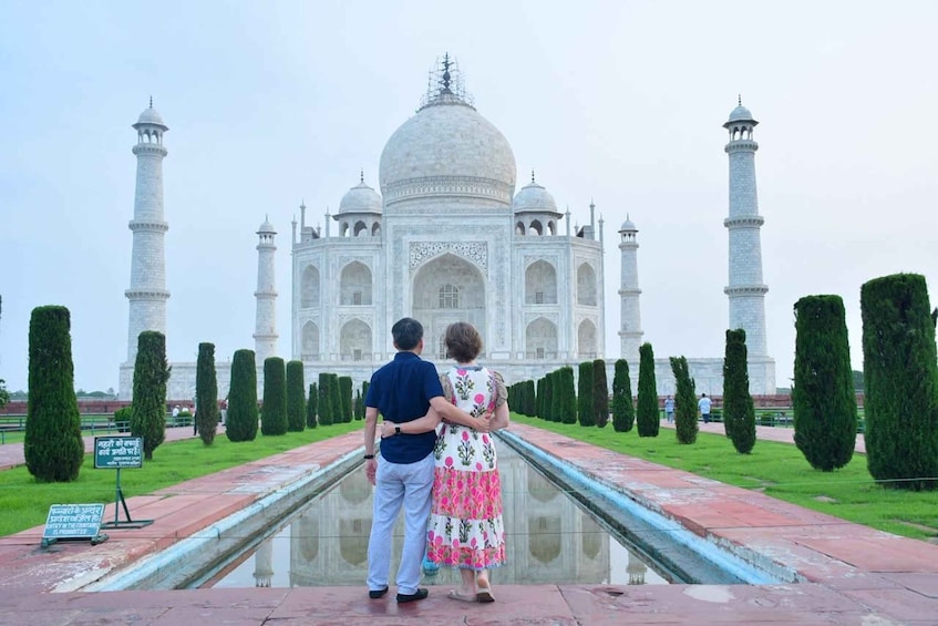 A couple standing in front of the Taj Mahal, with a reflection in the water. 1