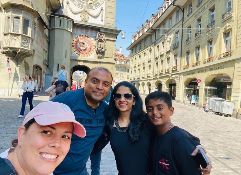 A group of people posing in front of a historic building with ornate clocks and a pharmacy sign. 3