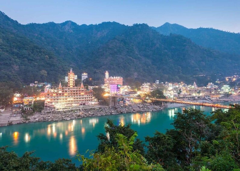 A riverside town with illuminated buildings and a mountainous backdrop. 1