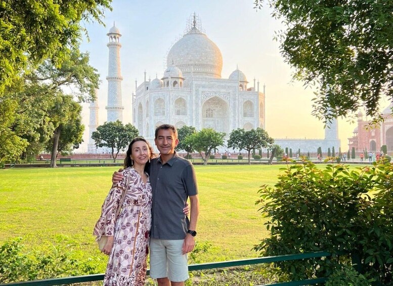 Una pareja parada frente al Taj Mahal, con un césped verde y árboles. 1