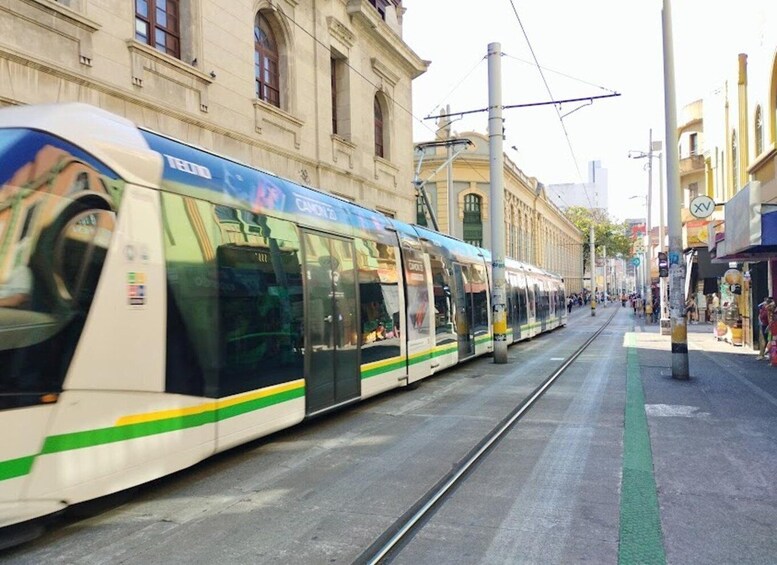 Un tram modern circula pel carrer d'una ciutat, amb edificis i botigues al voltant. 5