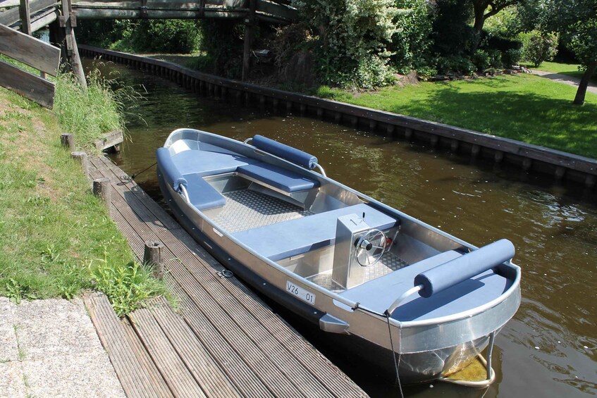 Ein schmaler Kanalboot liegt an einem hölzernen Steg, im Hintergrund Ufergrün und ein Kanal. 5
