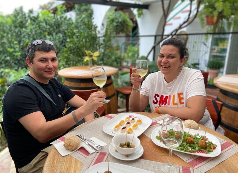 Two people sitting at an outdoor table with food and drinks. 1