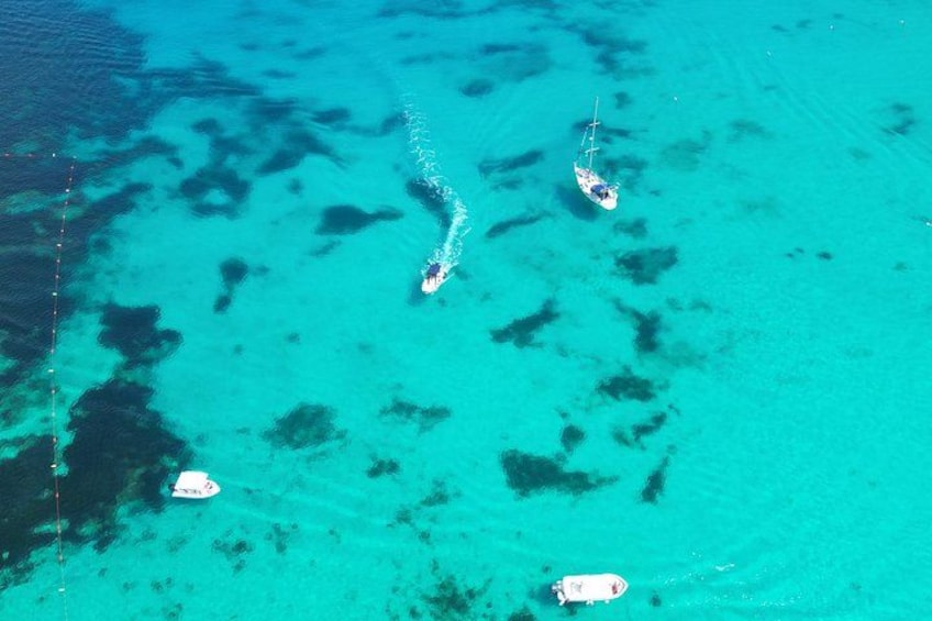 A turquoise sea with three boats, one anchored and two moving. 2