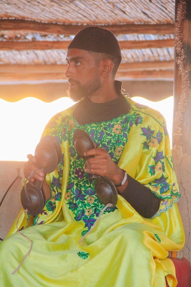 A person in a yellow garment with floral patterns, holding a pair of traditional leather shoes. 5
