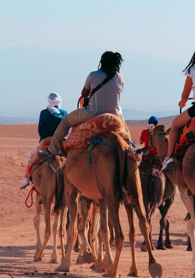 A group of people riding camels in a desert landscape. 1