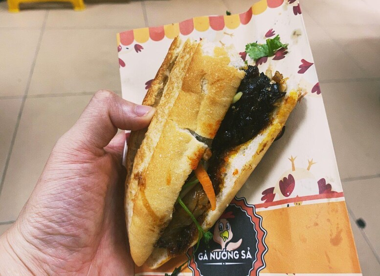 Una mano sosteniendo un sándwich con un envoltorio de papel que tiene un logotipo y texto. 2