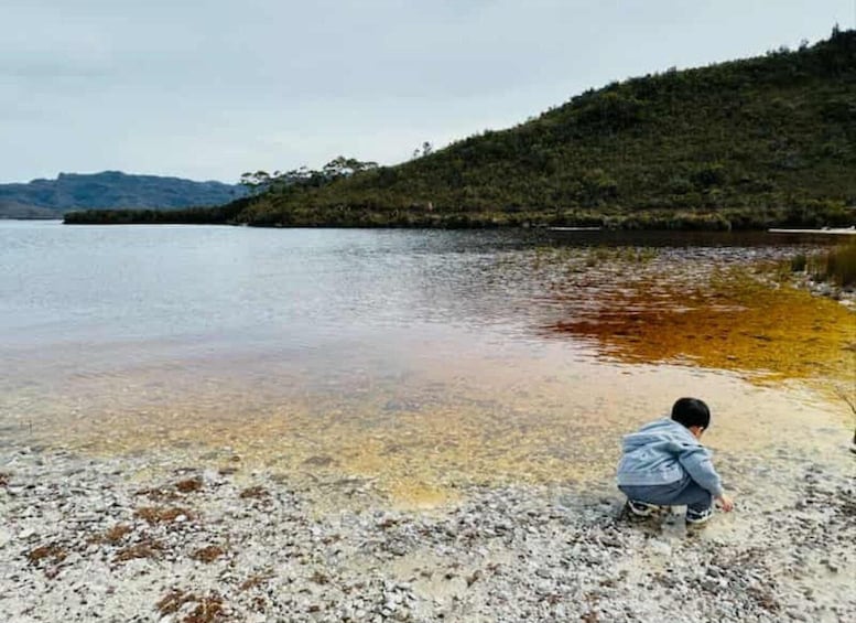 A child playing near a lake with clear water and a forested hill in the background. 5