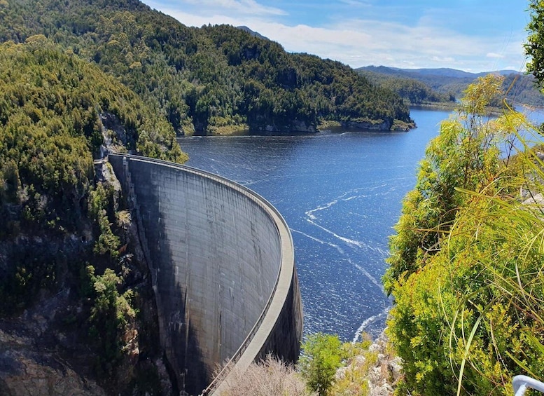 A large dam with a curved spillway, surrounded by dense forest and a calm lake. 4