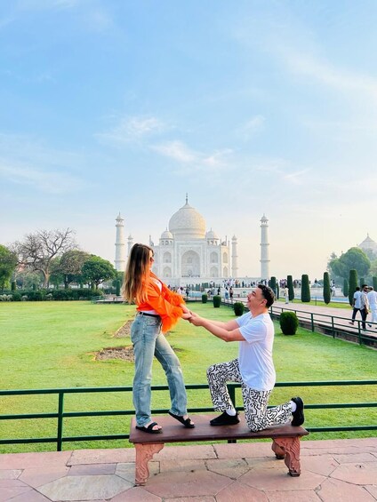 Zwei Personen sitzen auf einer Bank, im Hintergrund der Taj Mahal. 1