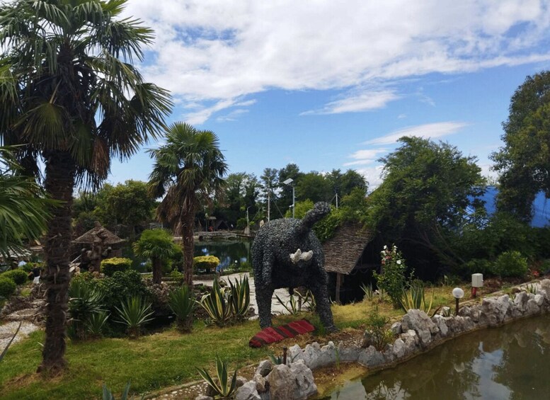 A garden with a large elephant statue, palm trees, a pond, and various plants. 2