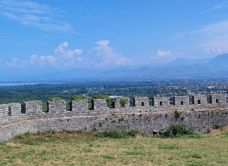 A stone wall with ruins, a cityscape, and mountains in the distance. 5