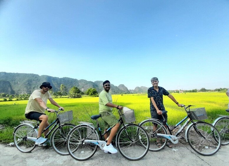 Three people on bicycles in a rural landscape with green fields and mountains in the background. 4