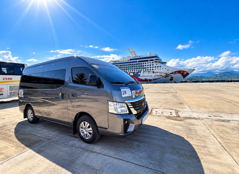 A silver van parked on a tarmac with a cruise ship in the background. 3