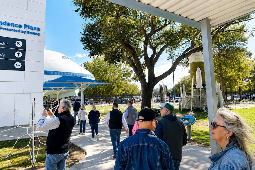 A group of people walking towards a large white building with a blue sign reading 'Independence Plaza Presented by Boeing'. 2