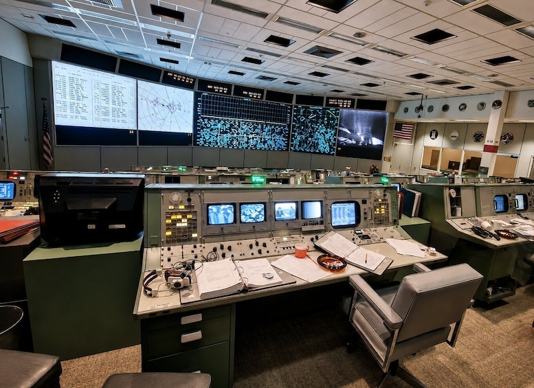 A control room with multiple monitors displaying data, control panels, and various technical equipment. 1