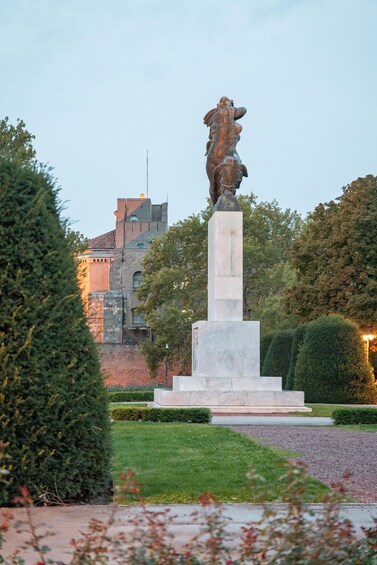 A bronze statue on a pedestal in a park with a building in the background. 5