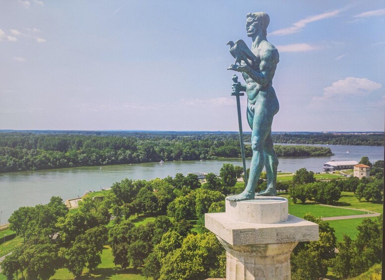 A bronze statue of a man holding a bird, overlooking a river and park. 2