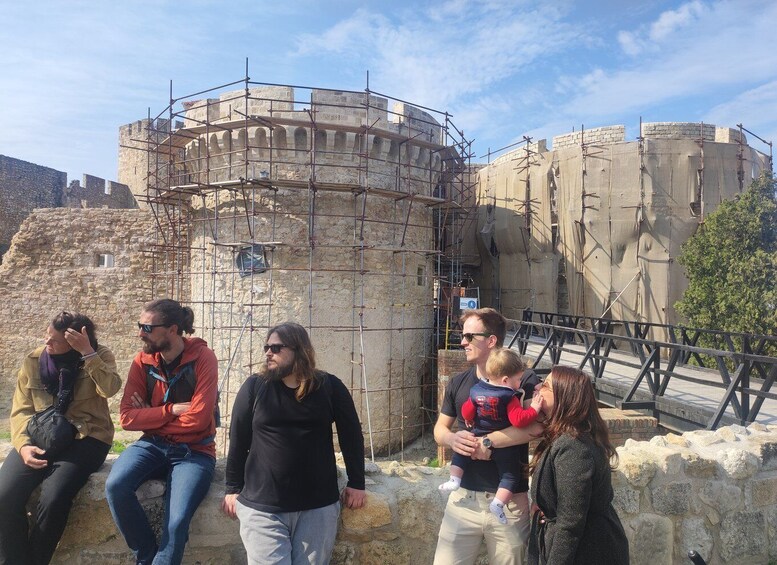 A group of people sitting on a stone wall in front of a historic building with scaffolding. 1