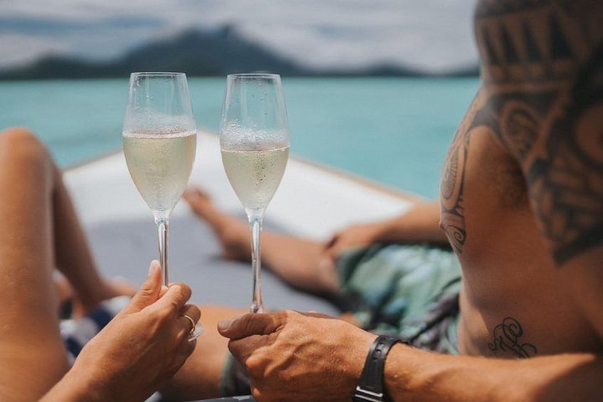 Twee personen proosten met champagnefluiten, met een waterlichaam en bergen op de achtergrond. 4