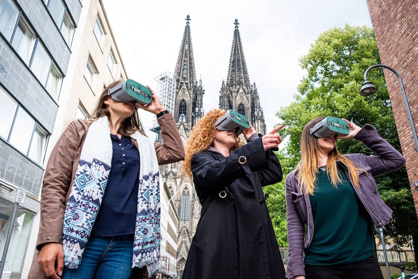 Drei Personen mit Virtual-Reality-Brillen vor einem gotischen Dom. 1