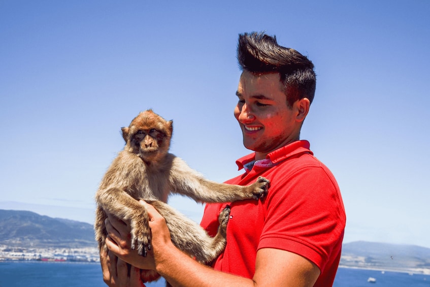 A person holding a monkey with a coastal landscape in the background. 2