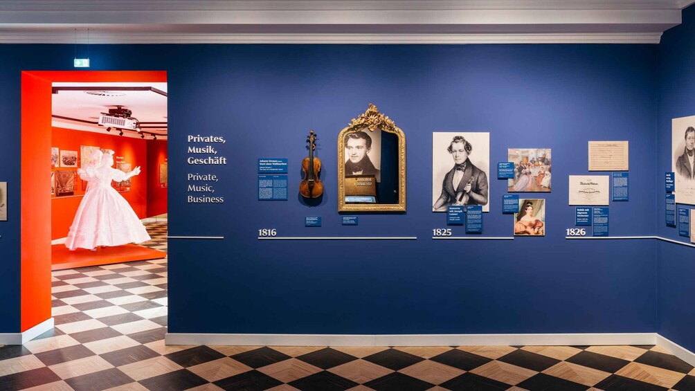 An exhibition with historical artifacts and information panels, including a violin, framed portrait, and documents. 2