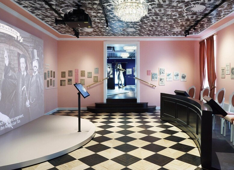 An art gallery with a checkered floor, a projector screen, and a staircase leading to another room. 4