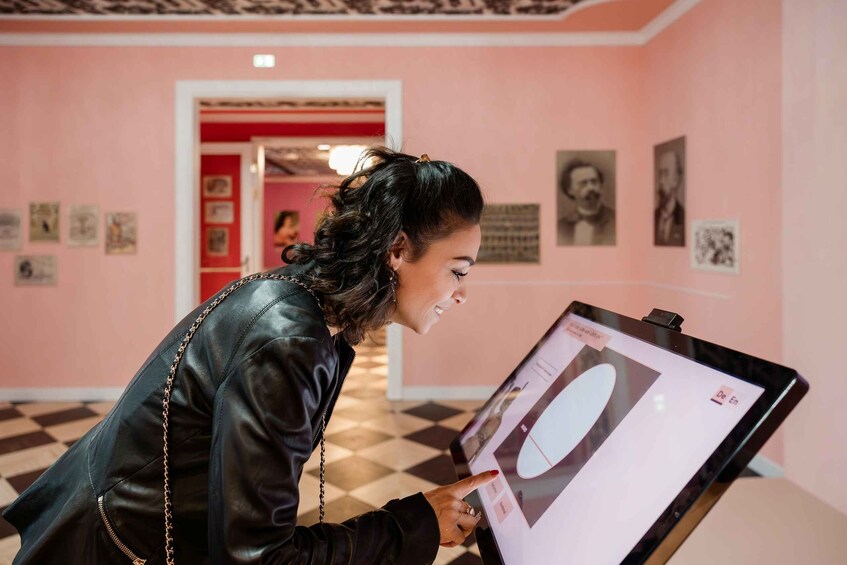 A person examining a digital display in a pink-walled room with framed pictures on the walls. 5