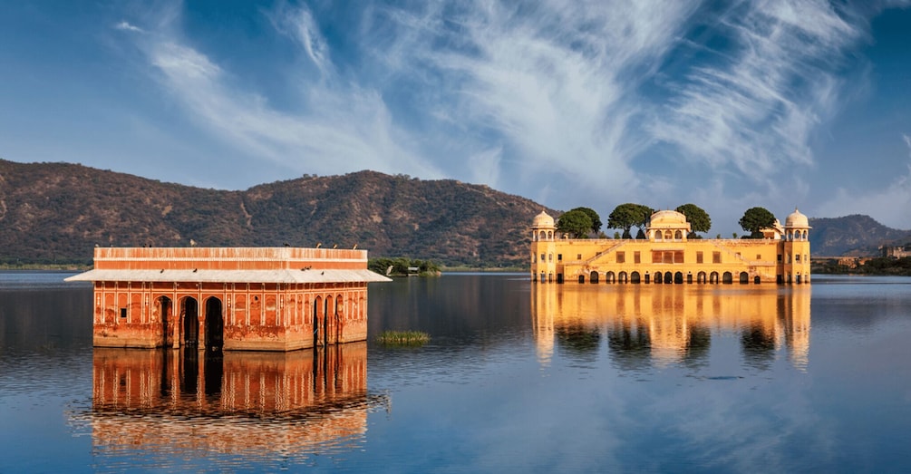 A historic building with a reflection in calm water, surrounded by mountains. 4