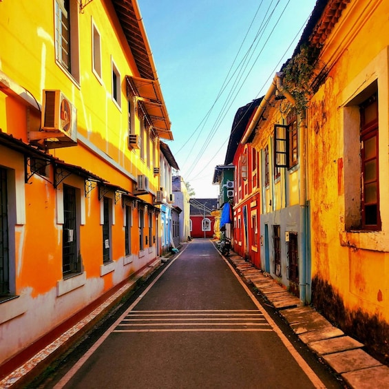 A narrow street flanked by colorful buildings with air conditioning units, a clear sky, and a blue tarp on a building. 4