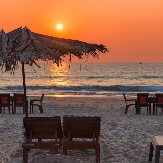 A beach with wooden chairs and a thatched umbrella under a sunset. 5