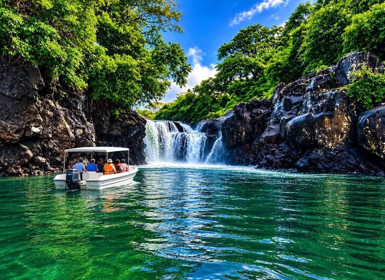 A boat with passengers near a waterfall surrounded by lush greenery. 1