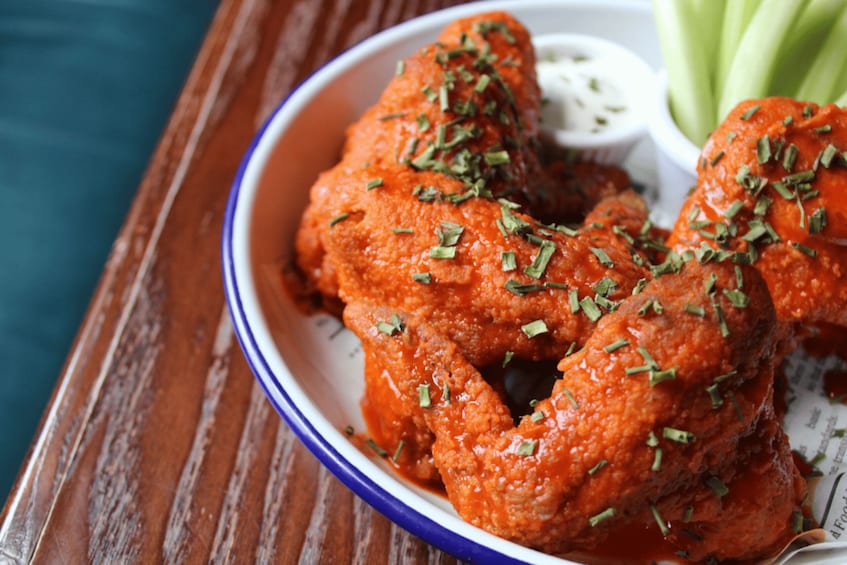A plate of buffalo wings with a blue rim, garnished with herbs, and accompanied by celery sticks and a small bowl of blue sauce. 2