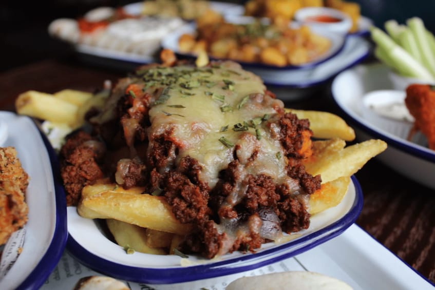 A dish of meat topped with cheese and herbs, accompanied by fries and dipping sauces. 5