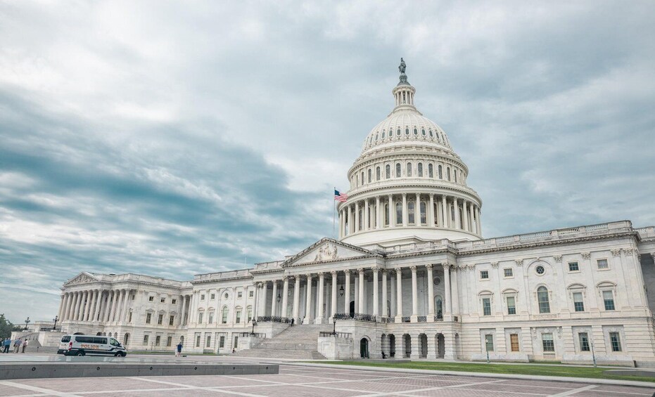 A large white building with a dome and columns, likely a government building, under a cloudy sky. 1