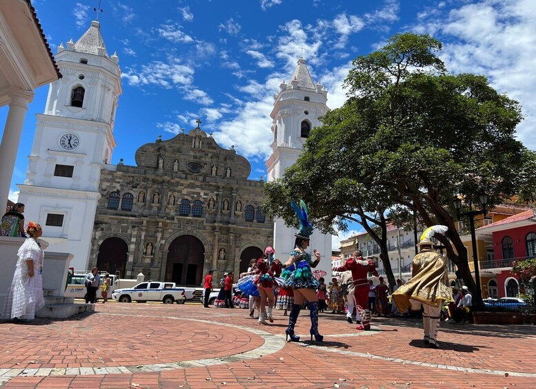 A historic building with two towers and a clock, surrounded by a plaza with people in traditional costumes. 3