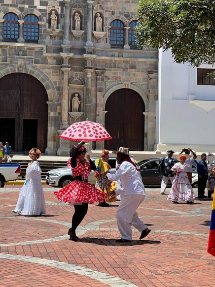 A group of people dancing in traditional attire in front of a historic building with arched windows and statues. 4