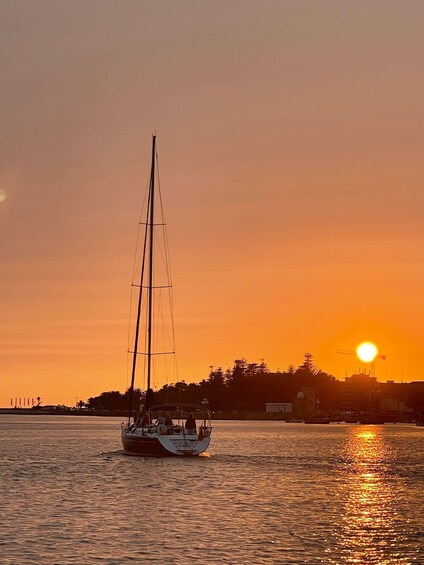 Un velero en aguas tranquilas durante el atardecer, con un horizonte urbano al fondo. 2