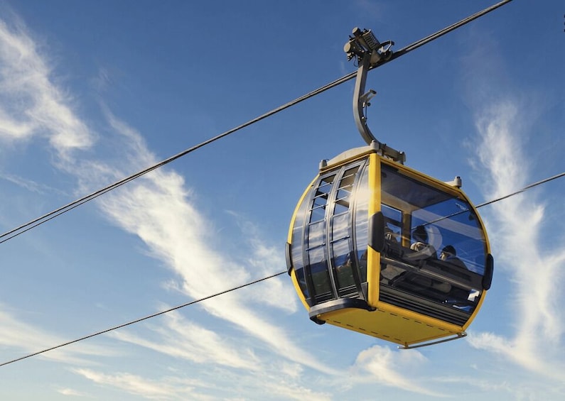 A yellow cable car suspended by cables against a clear blue sky with scattered clouds. 5