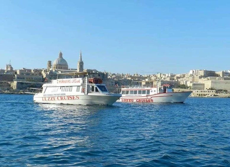 Two cruise boats named 'Luzzu Cruises' on the water with a cityscape in the background. 2