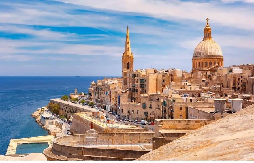 A coastal cityscape with historic architecture, including a prominent church with a dome and a tall bell tower. 3