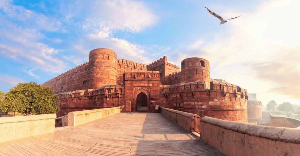 A historic fort with a large entrance, a bridge leading to it, and a bird flying in the sky. 2