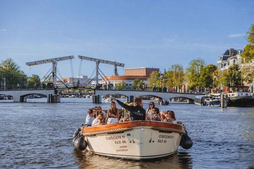 A boat with passengers on a canal, a bridge, and buildings in the background. 5