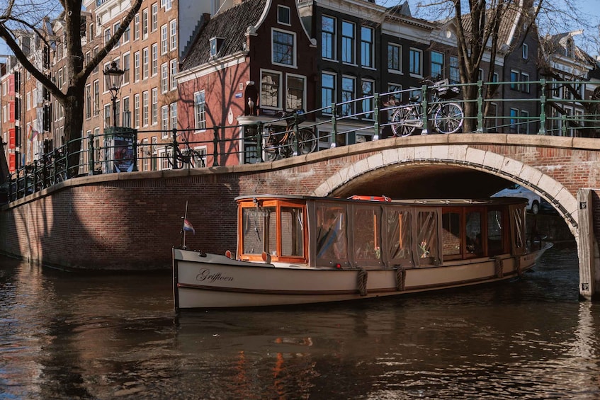 A canal boat named 'Griffioen' docked under a bridge with bicycles parked on the bridge. 1